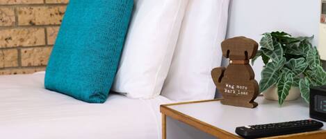 Un letto con cuscini bianchi e color acquamarina, una piccola statuina di un orso di legno, una pianta e un telecomando su un comodino.