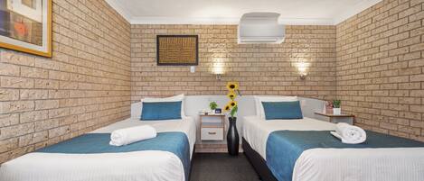 Camera d'albergo con due letti, un muro in mattoni, un quadro incorniciato e un vaso con girasoli.