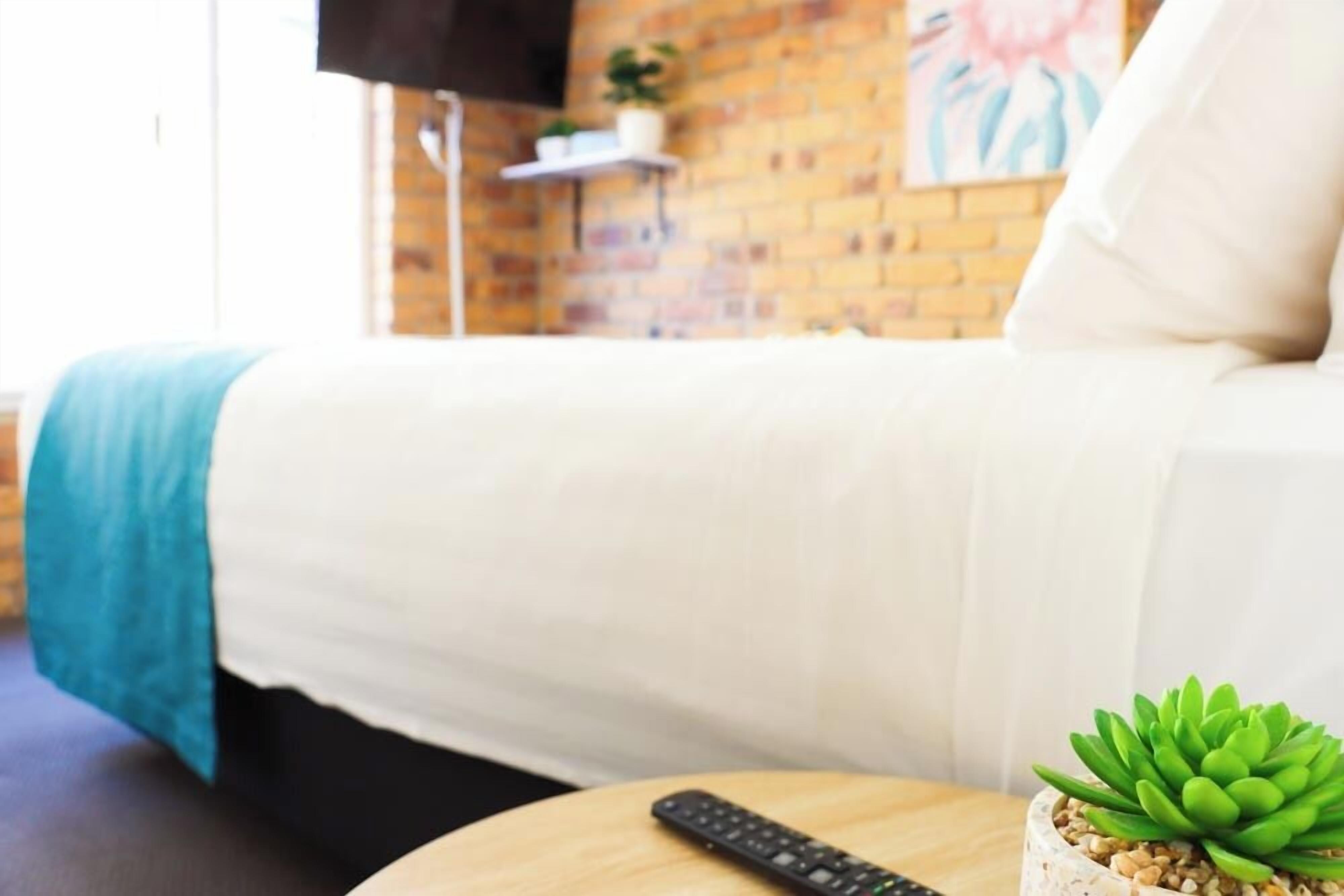 A bedroom with a bed, a remote control, and a potted plant on a round table.
