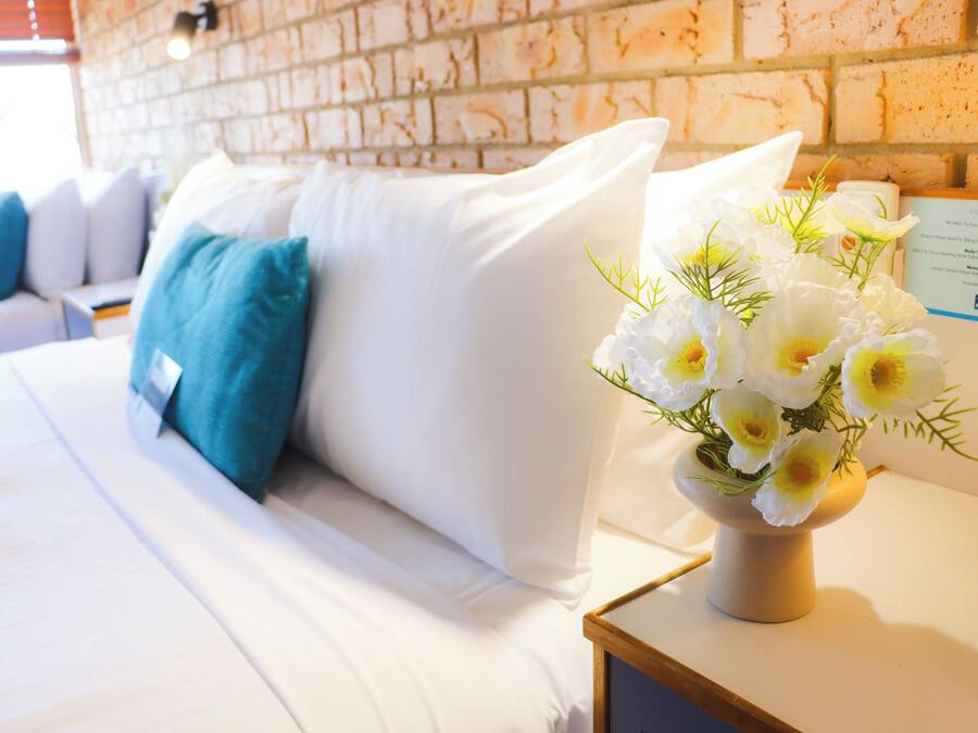 Una habitación de hotel con una cama, almohadas y un jarrón de flores en la mesita de noche.
