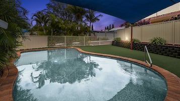 Una piscina con borde de ladrillo, rodeada de una valla y follaje.