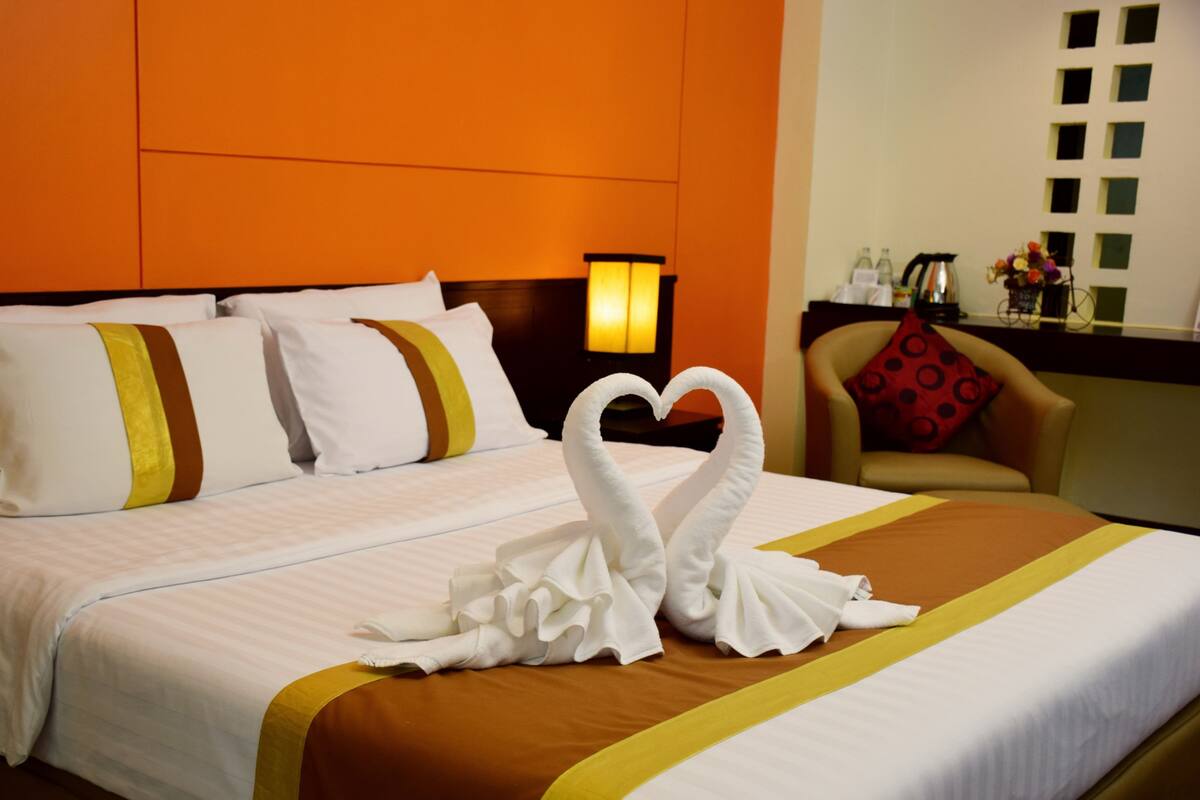 A hotel room with a bed, pillows, a nightstand, a lamp, and a chair.