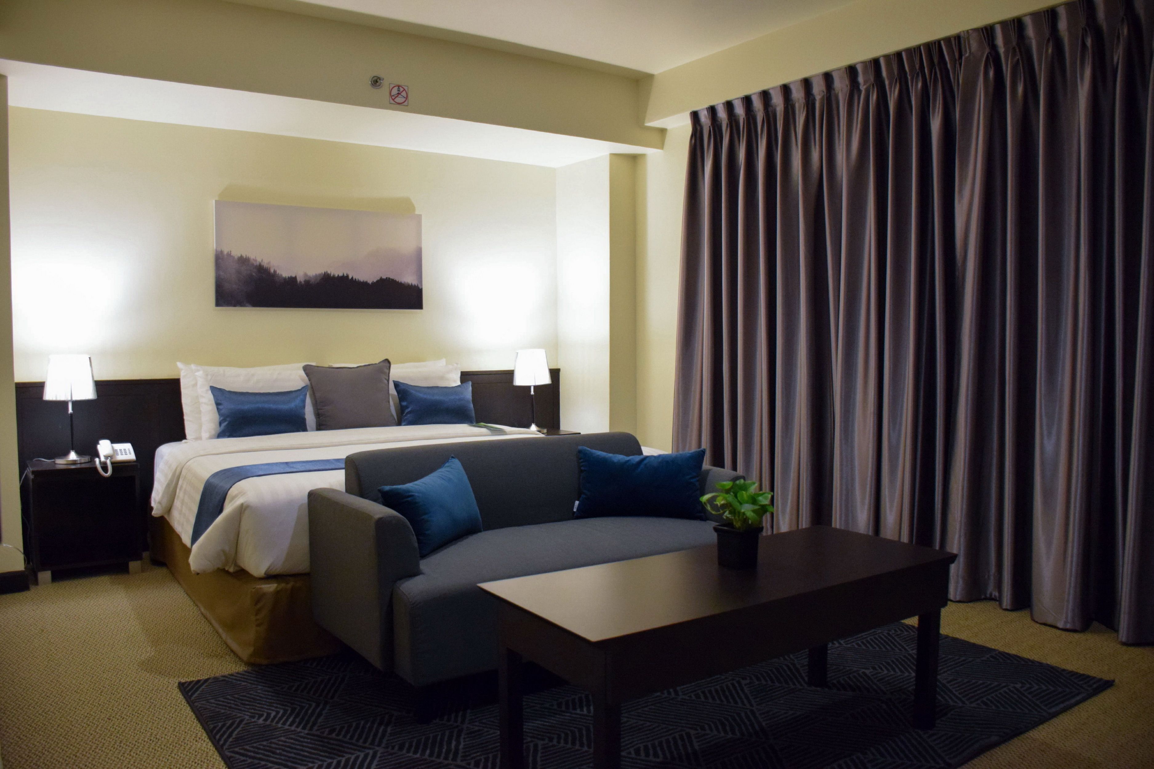 A hotel room with a bed, a sofa, a table, and a painting on the wall.