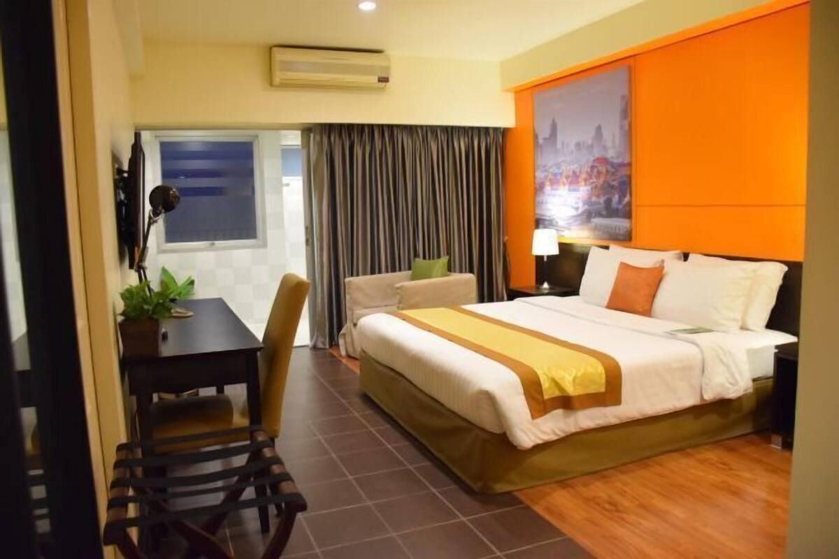 A hotel room with a bed, a desk, a chair, a window, and an air conditioning unit.
