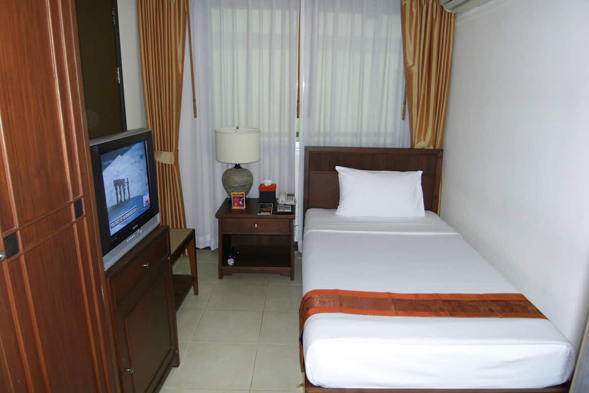 Een hotelkamer met een bed, een televisie, een nachtkastje, een lamp en gordijnen.