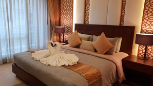 Een hotelkamer met een groot bed, een decoratieve zwaan van handdoek, behang met patroon en een nachtkastje met een lamp.