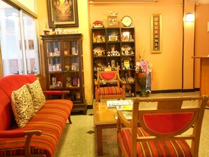 Uma sala de estar aconchegante com um sofá vermelho, uma poltrona de madeira e uma estante repleta de diversos objetos.