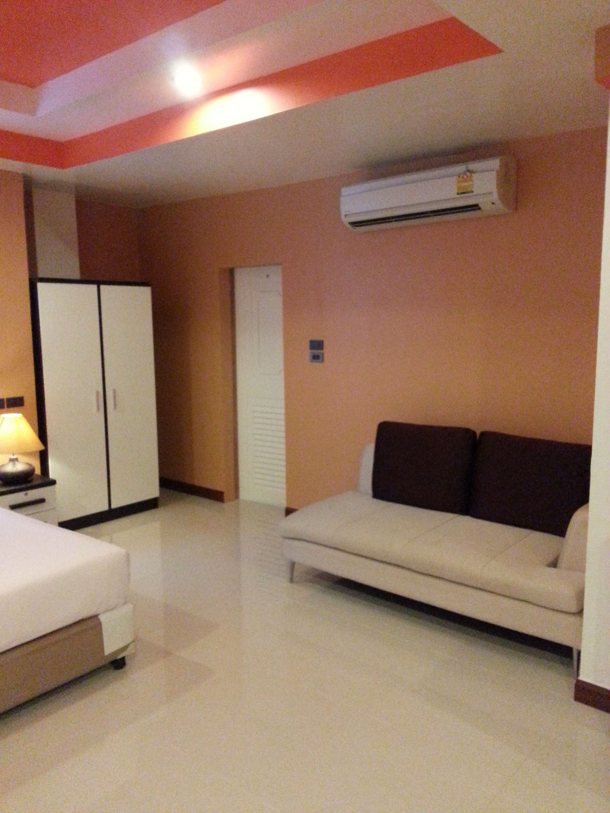 A hotel room with a bed, a sofa, a wardrobe, and an air conditioning unit.
