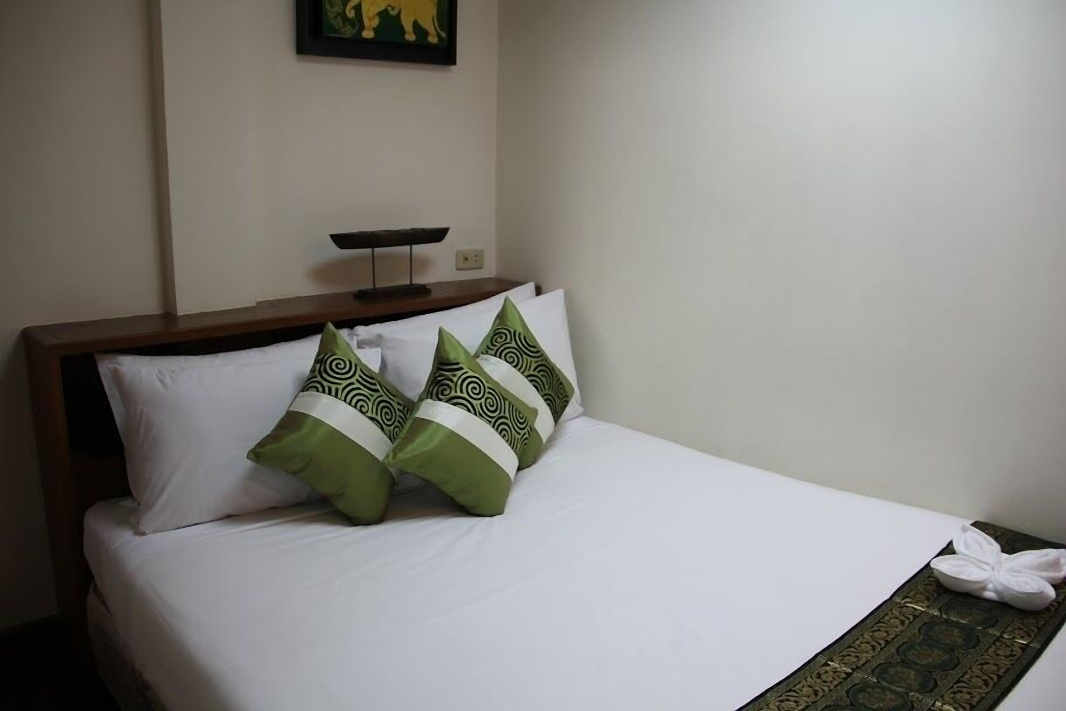 A neatly made bed with white bedding and two decorative pillows with green and black patterns.