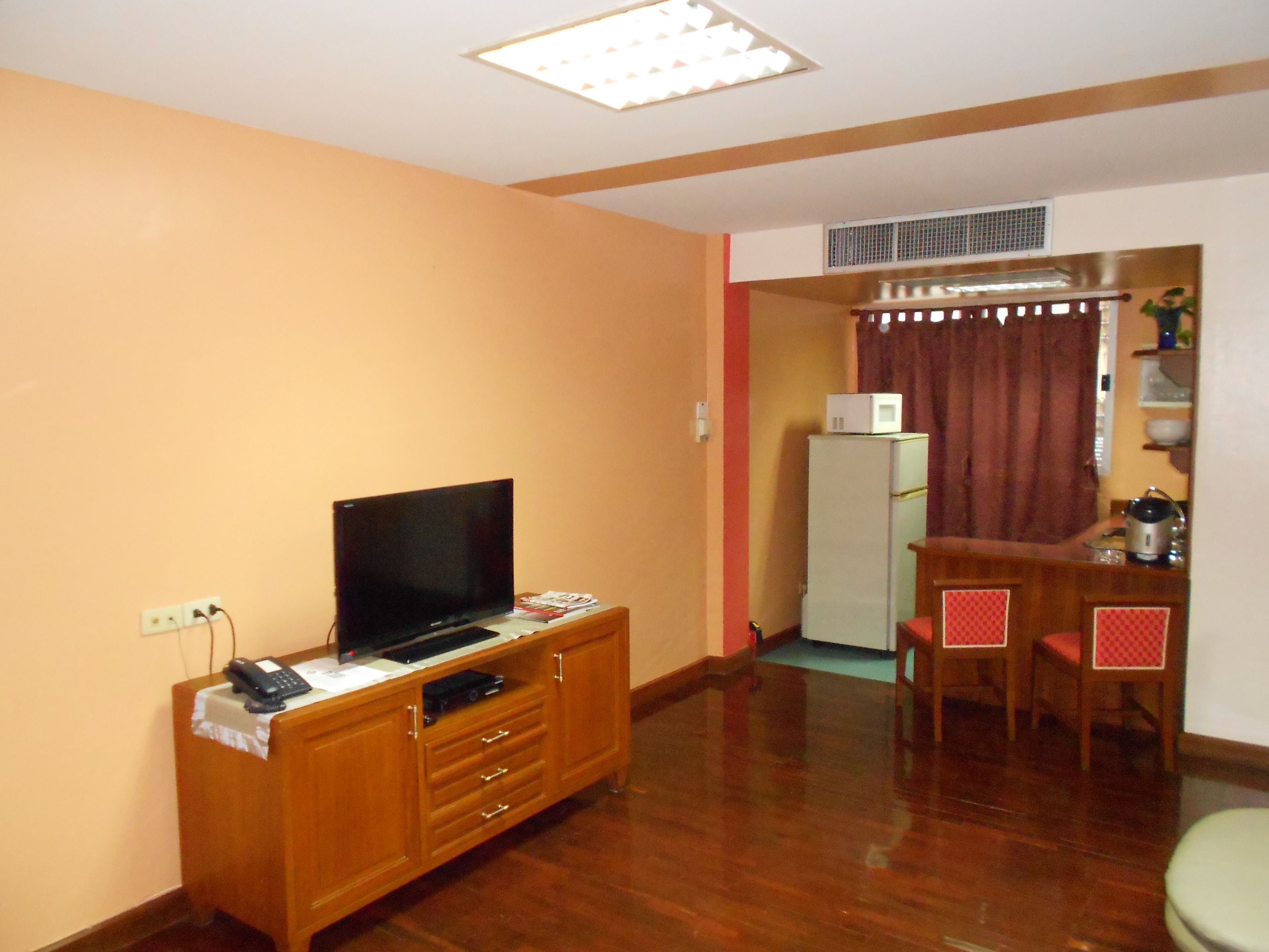 A compact living space with a television on a wooden cabinet, a refrigerator, and a dining area with chairs.