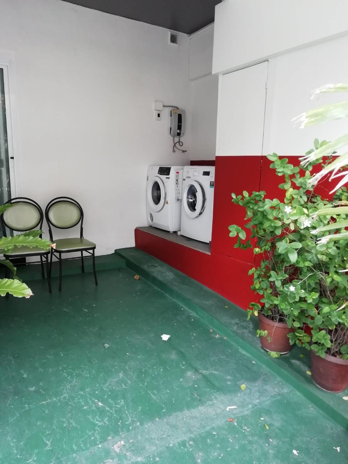 A small laundry area with two washing machines, two chairs, and a potted plant.