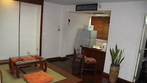 Ein traditioneller japanischer Raum mit Tatami-Boden, einem niedrigen Holztisch mit Kissen, einer kleinen Sitzecke und einer Topfpflanze.