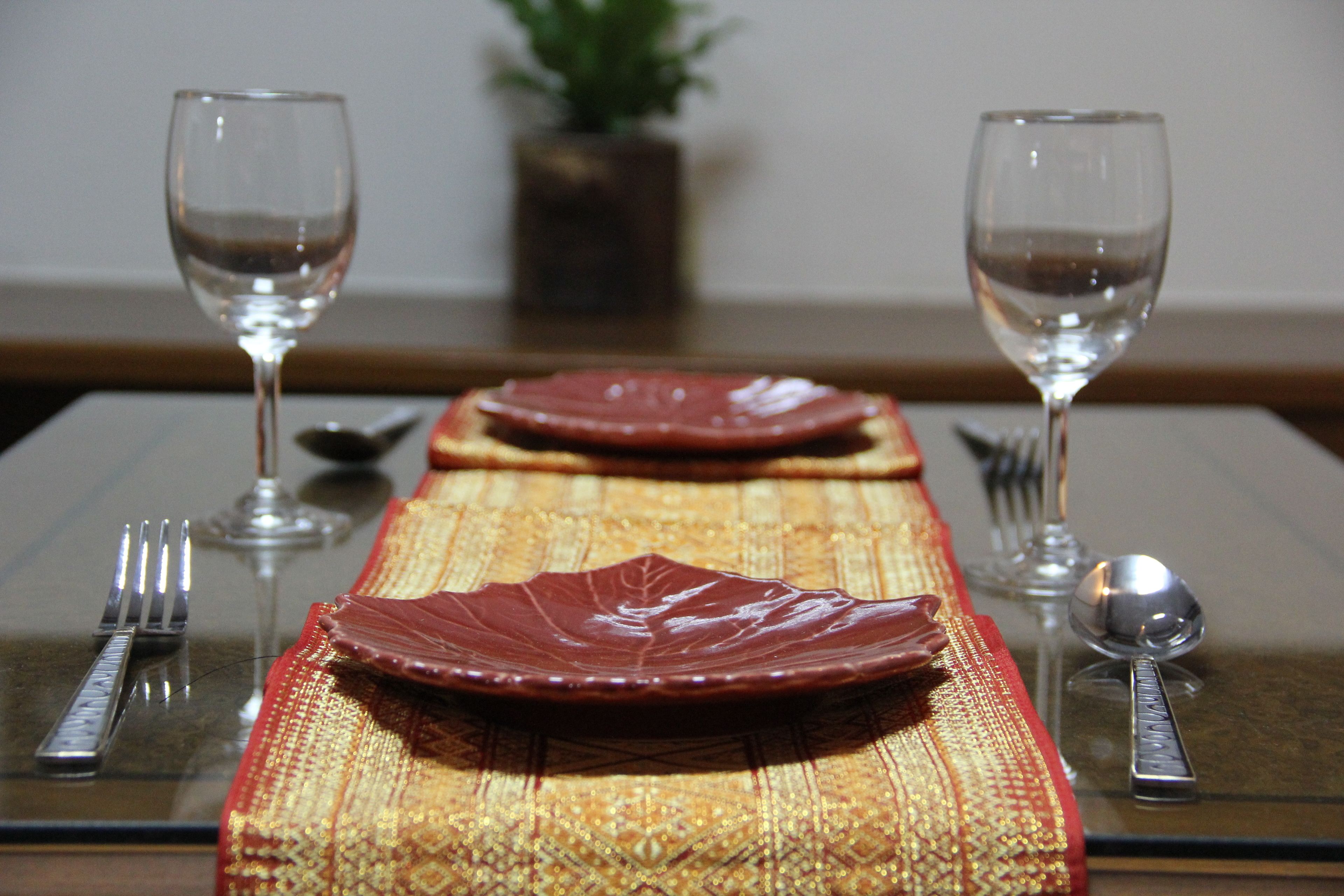 A dining table with a red plate, a fork, a spoon, and two wine glasses.