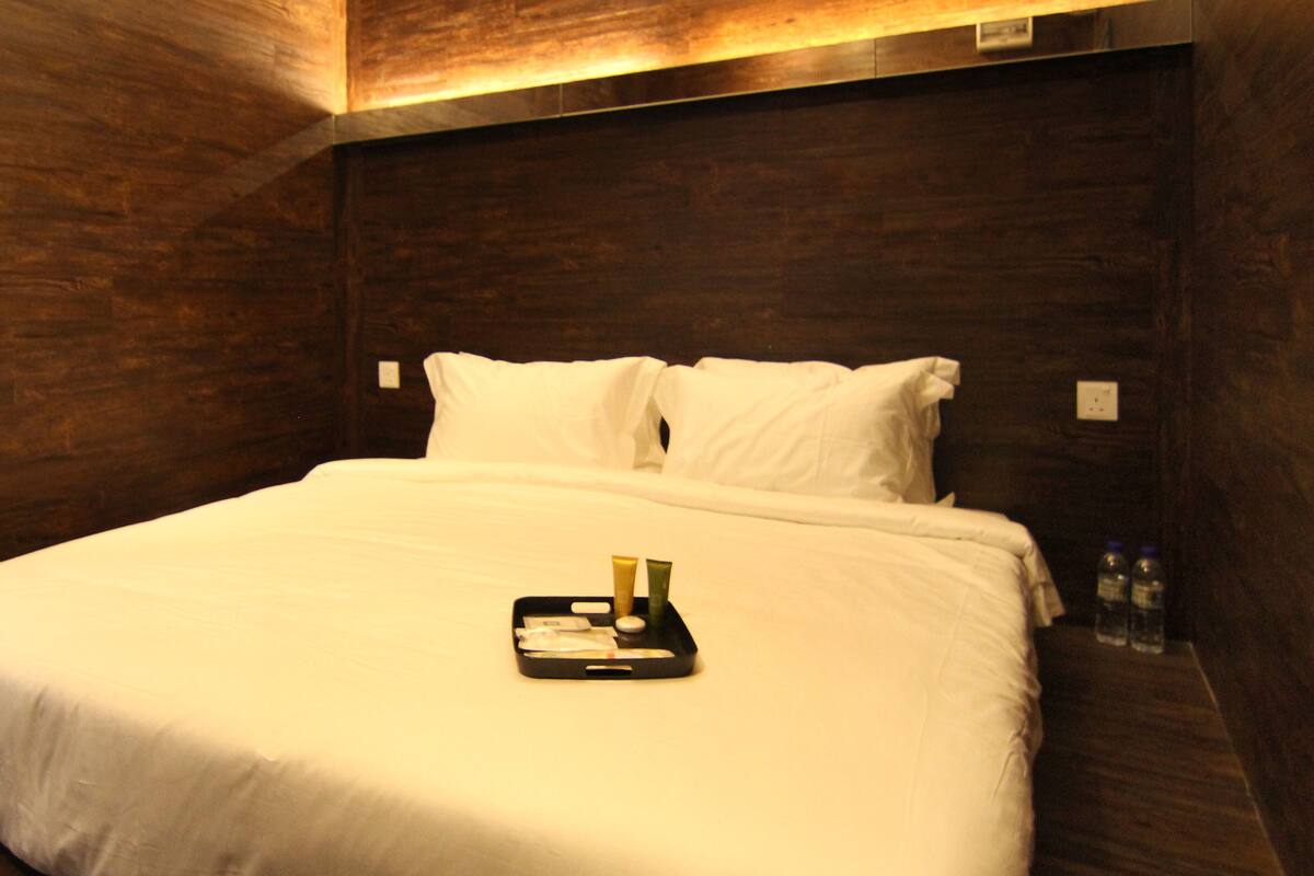 A neatly made bed with white linens, a tray with toiletries, and a bottle of water on the side.