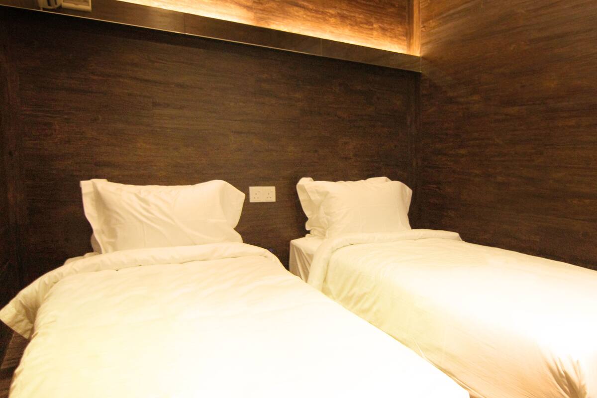 A room with two single beds, wooden walls, and a light fixture above.