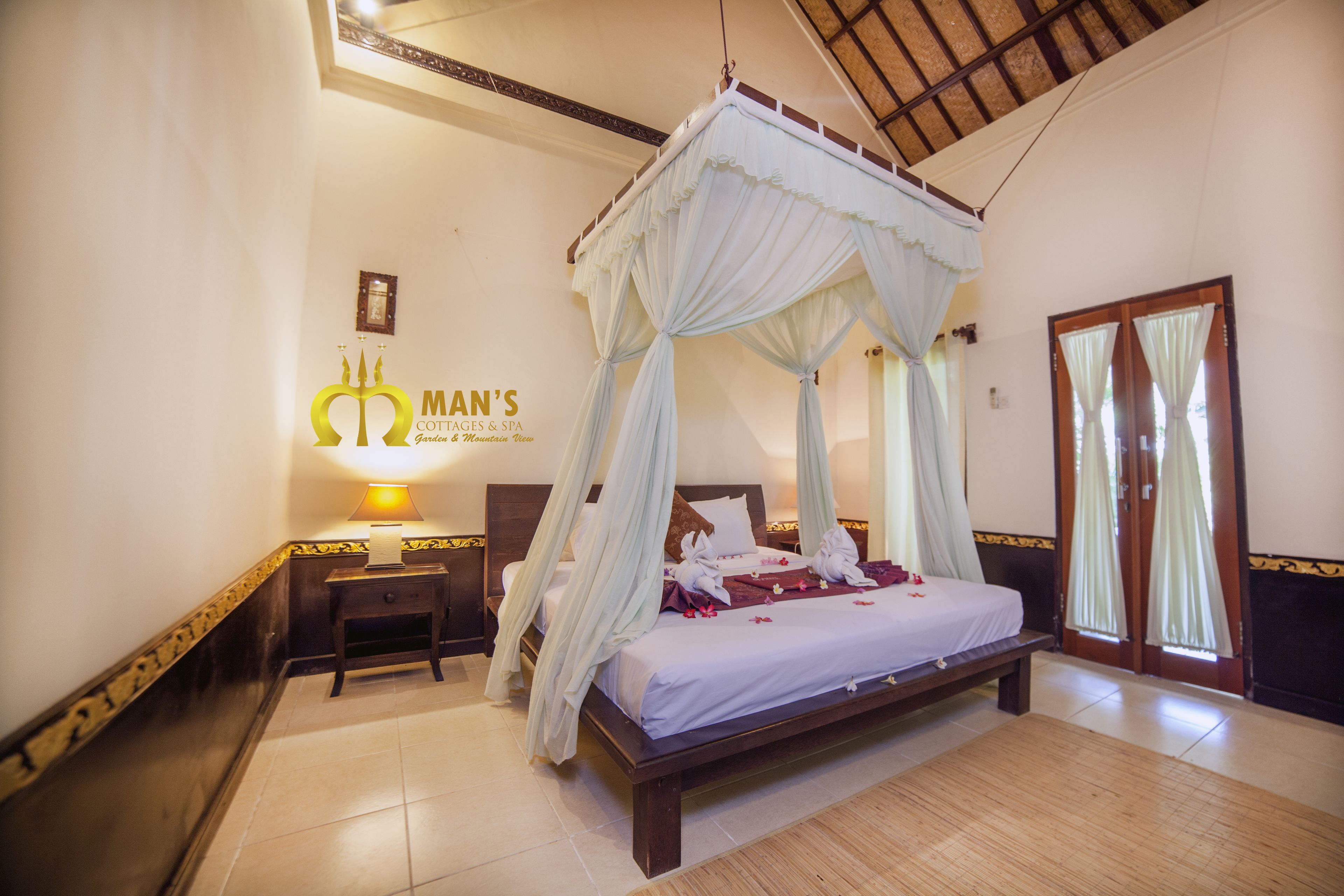 Una cama con dosel y cortina blanca, una mesita de noche con lámpara, y un cartel que dice "MAN'S COTTAGES & SPA".