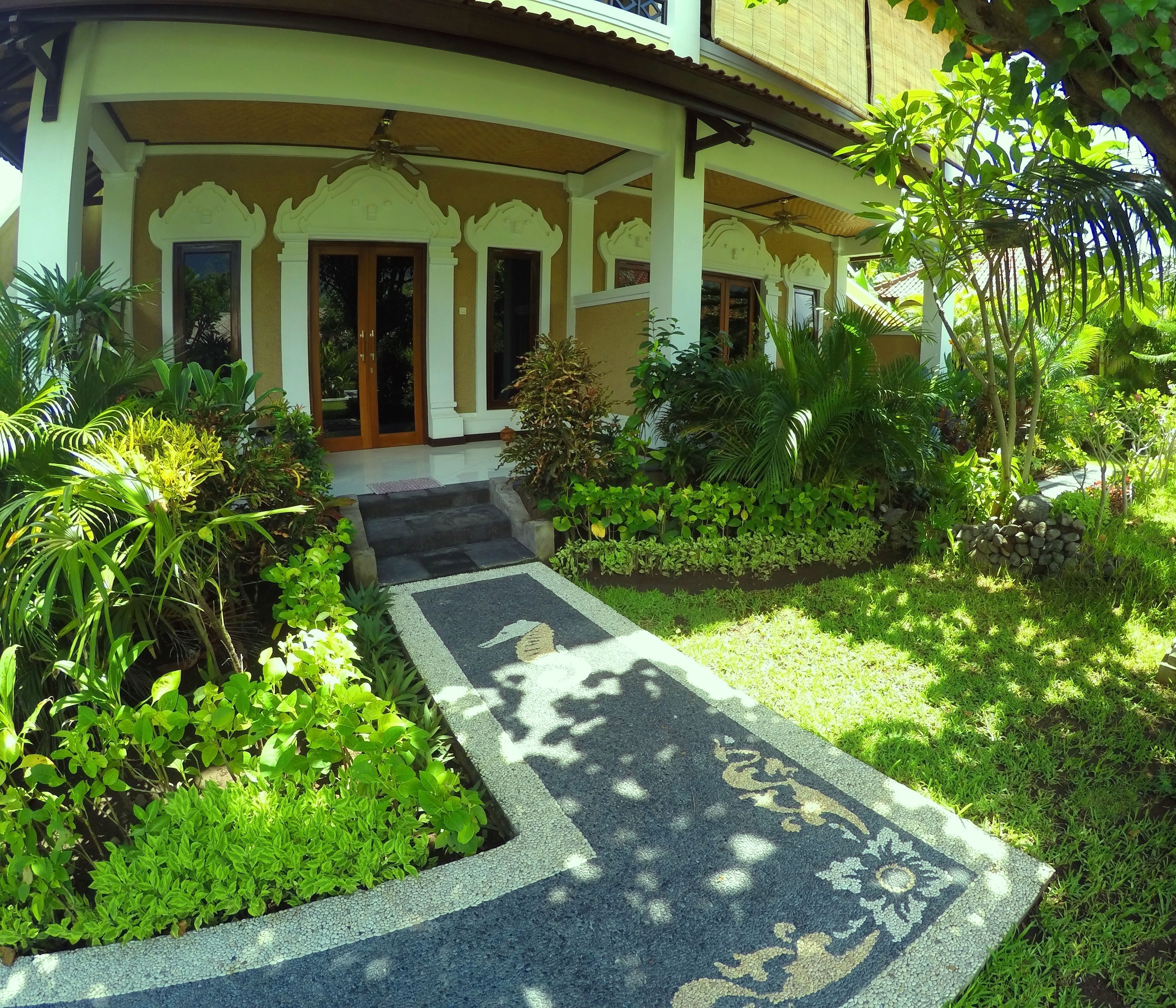 A building with a covered entrance, a paved pathway leading to the door, and surrounding greenery.