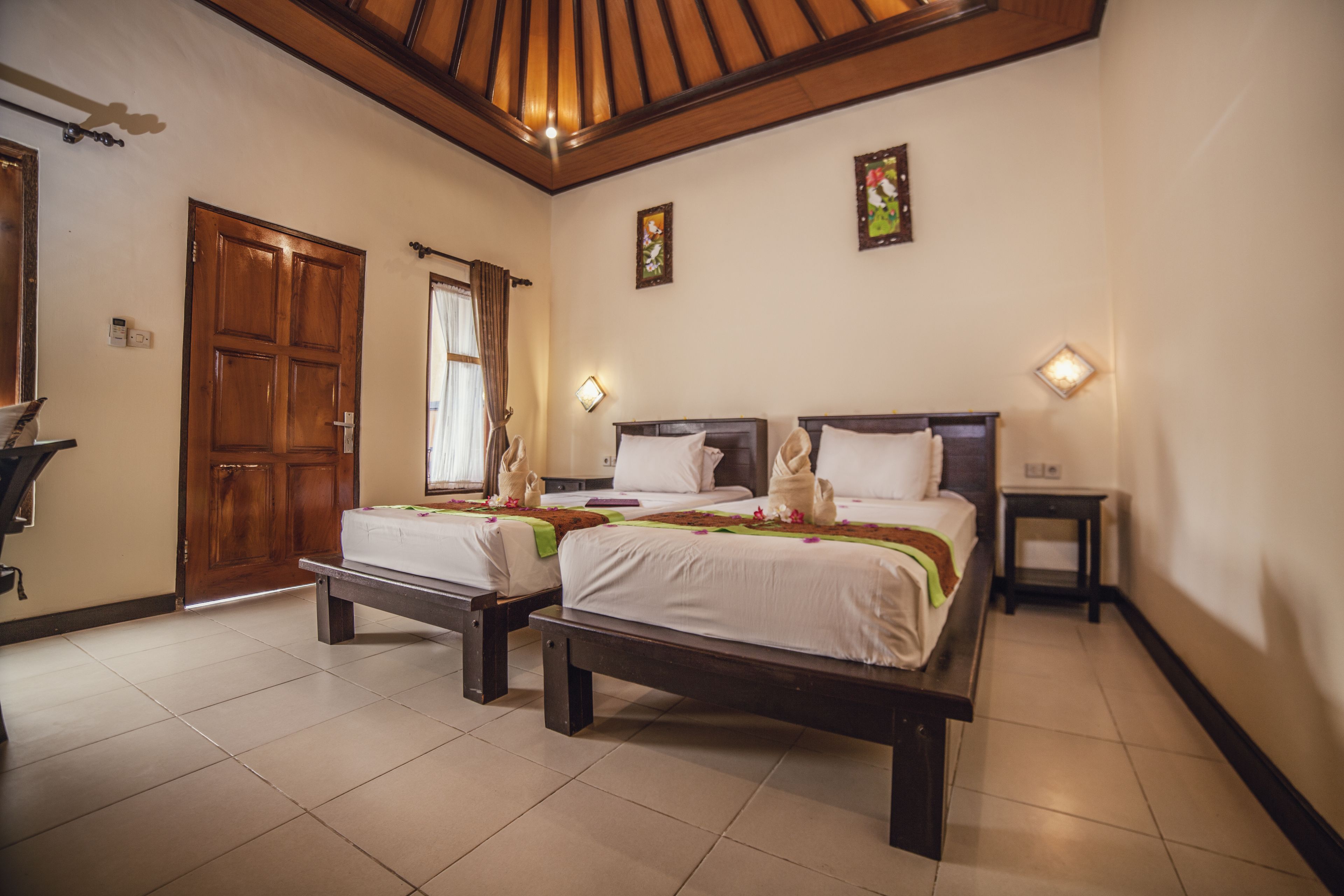 A hotel room with two beds, a wooden ceiling, and a large door.