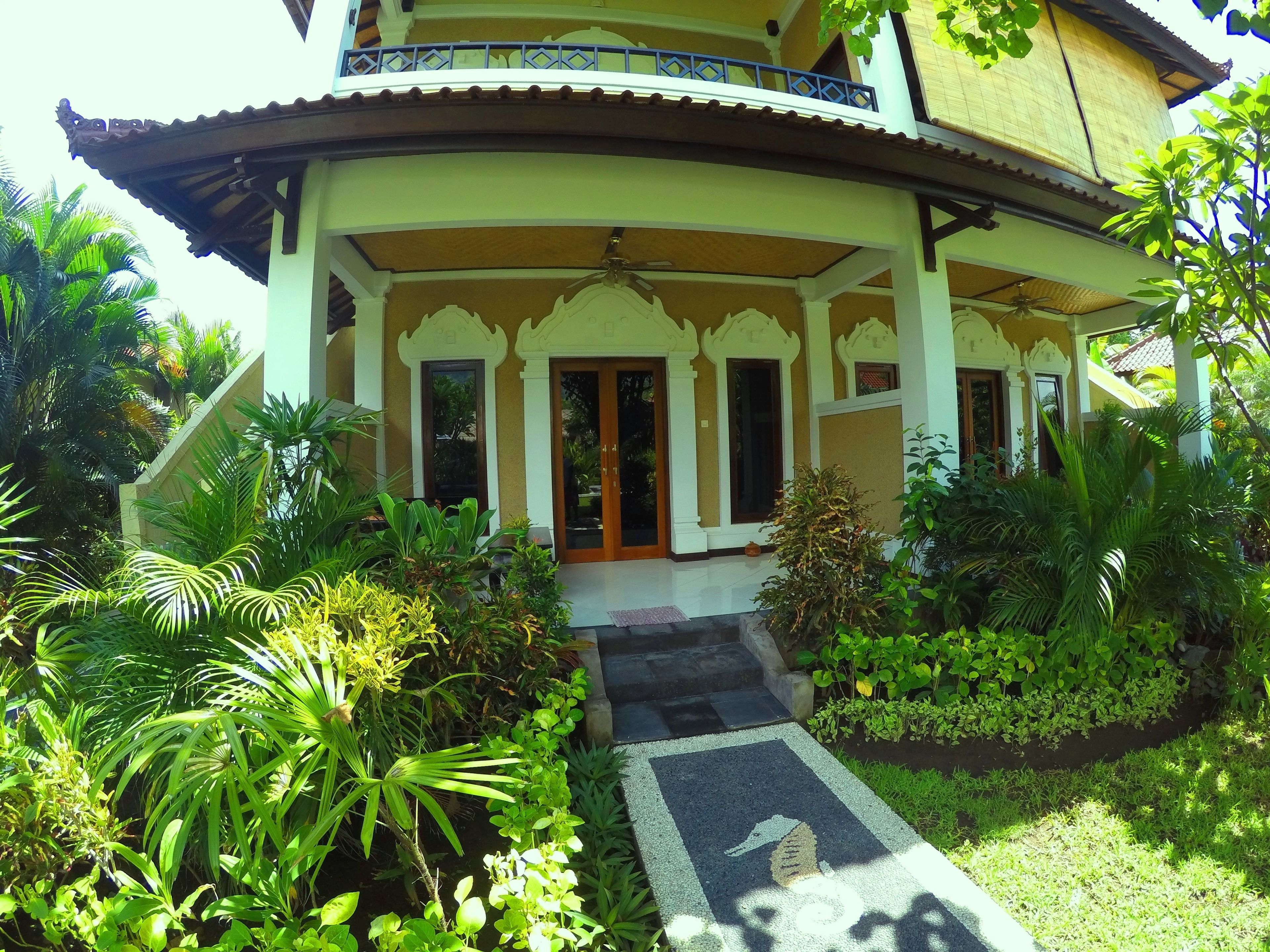 A traditional building with a covered entrance, steps leading up to it, and lush greenery surrounding the area.