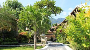 A curved pathway lined with lush greenery and a stone lantern. - Man's Cottages and Spa (Pemuteran)