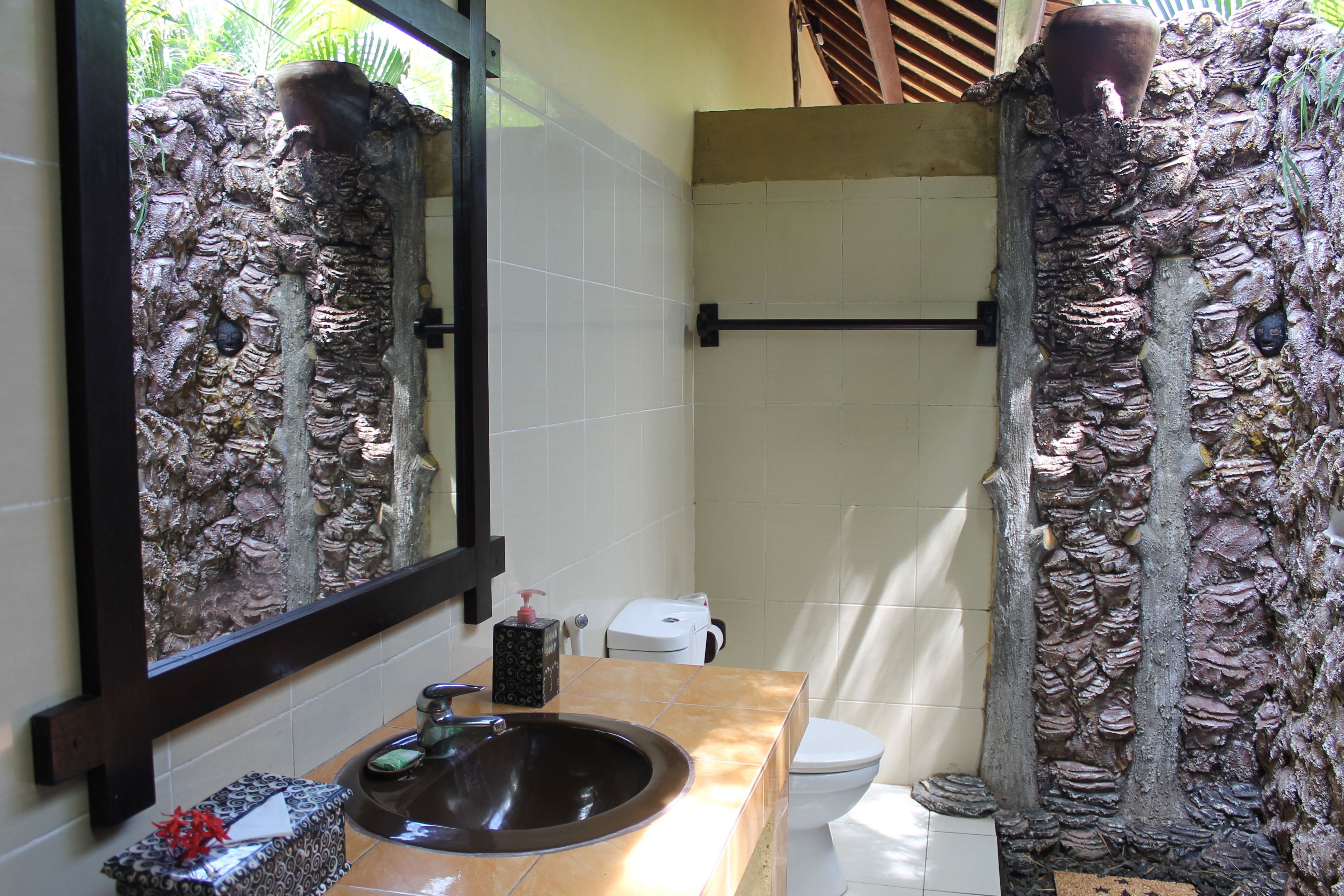 A bathroom with a stone wall, a sink, a mirror, and a toilet.