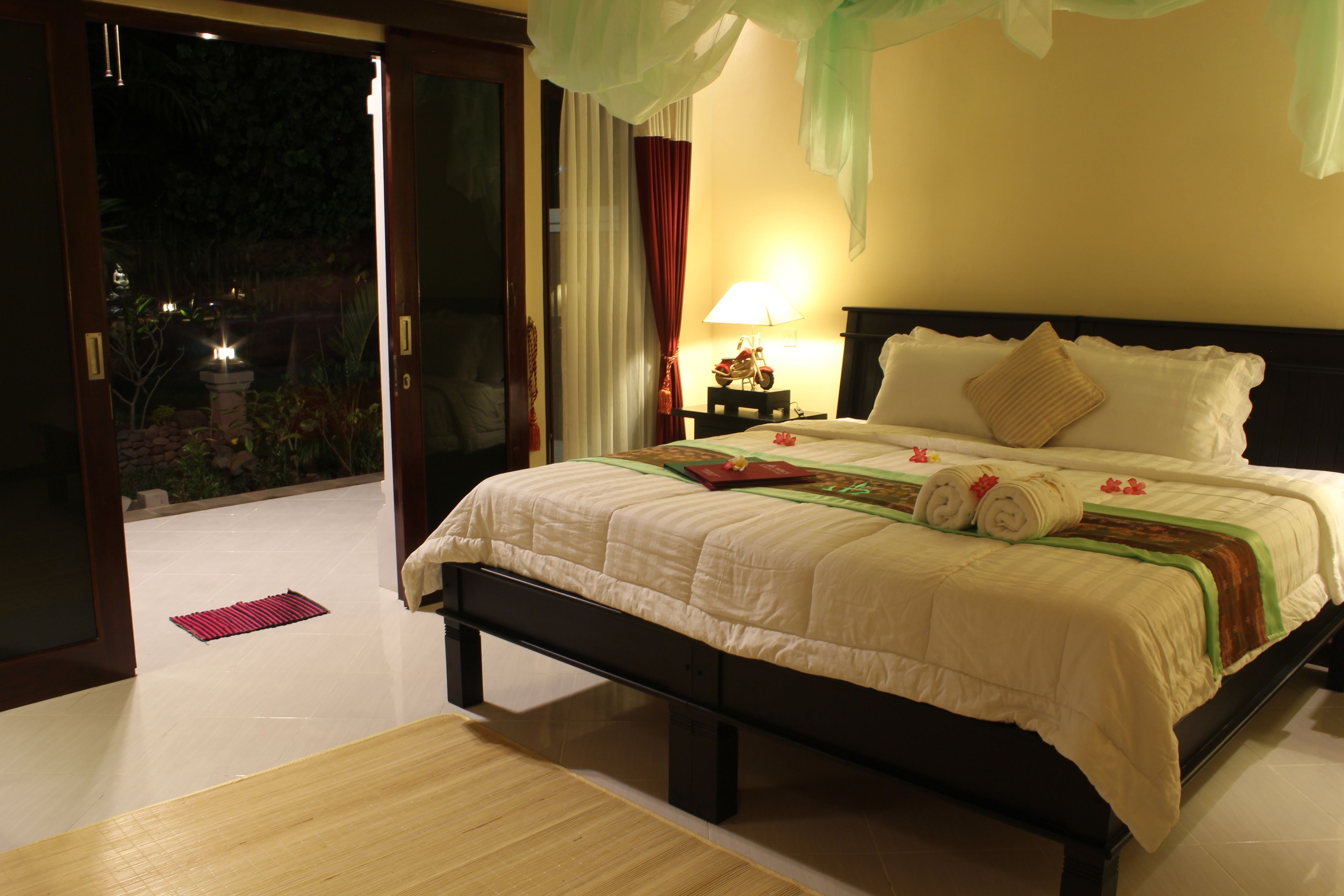 Un dormitorio bien iluminado con una cama grande, una mesita de noche con lámpara y vistas al exterior.