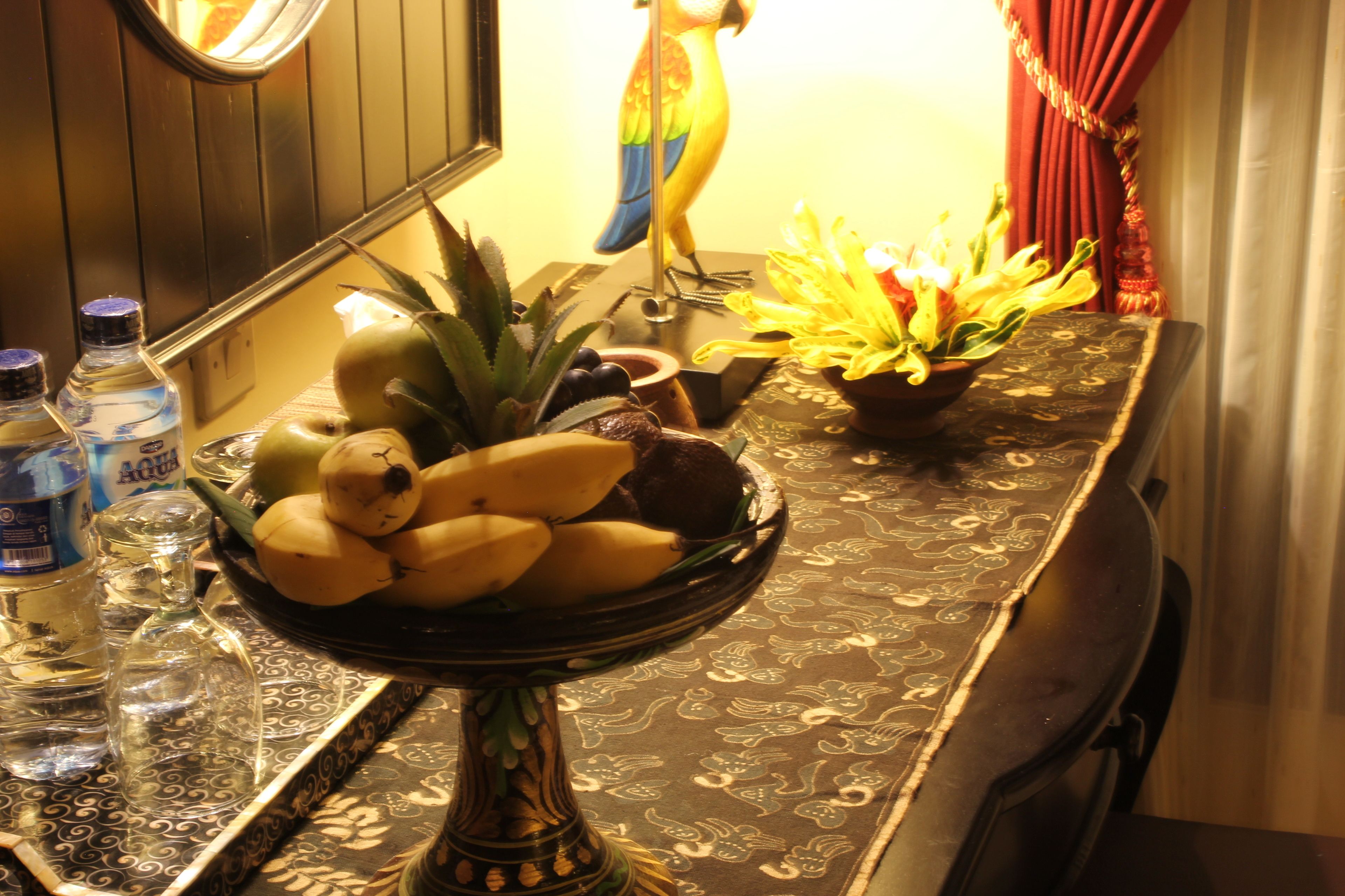 A table with a fruit bowl, a decorative bird, and a vase of flowers.