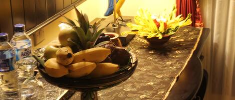 A table with a fruit bowl, a decorative bird, and a vase of flowers.