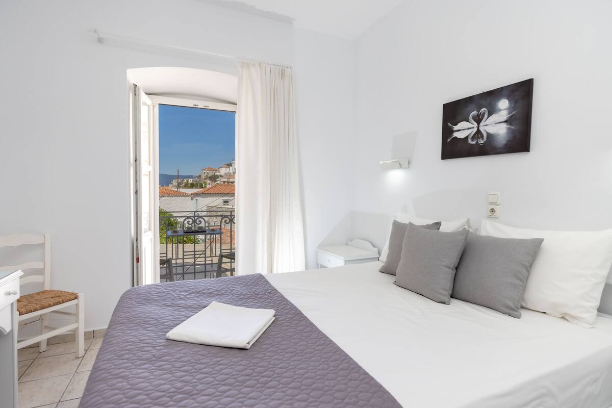 Une chambre d’hôtel avec un lit, une chaise, une table de chevet, un tableau et une vue sur l’extérieur.