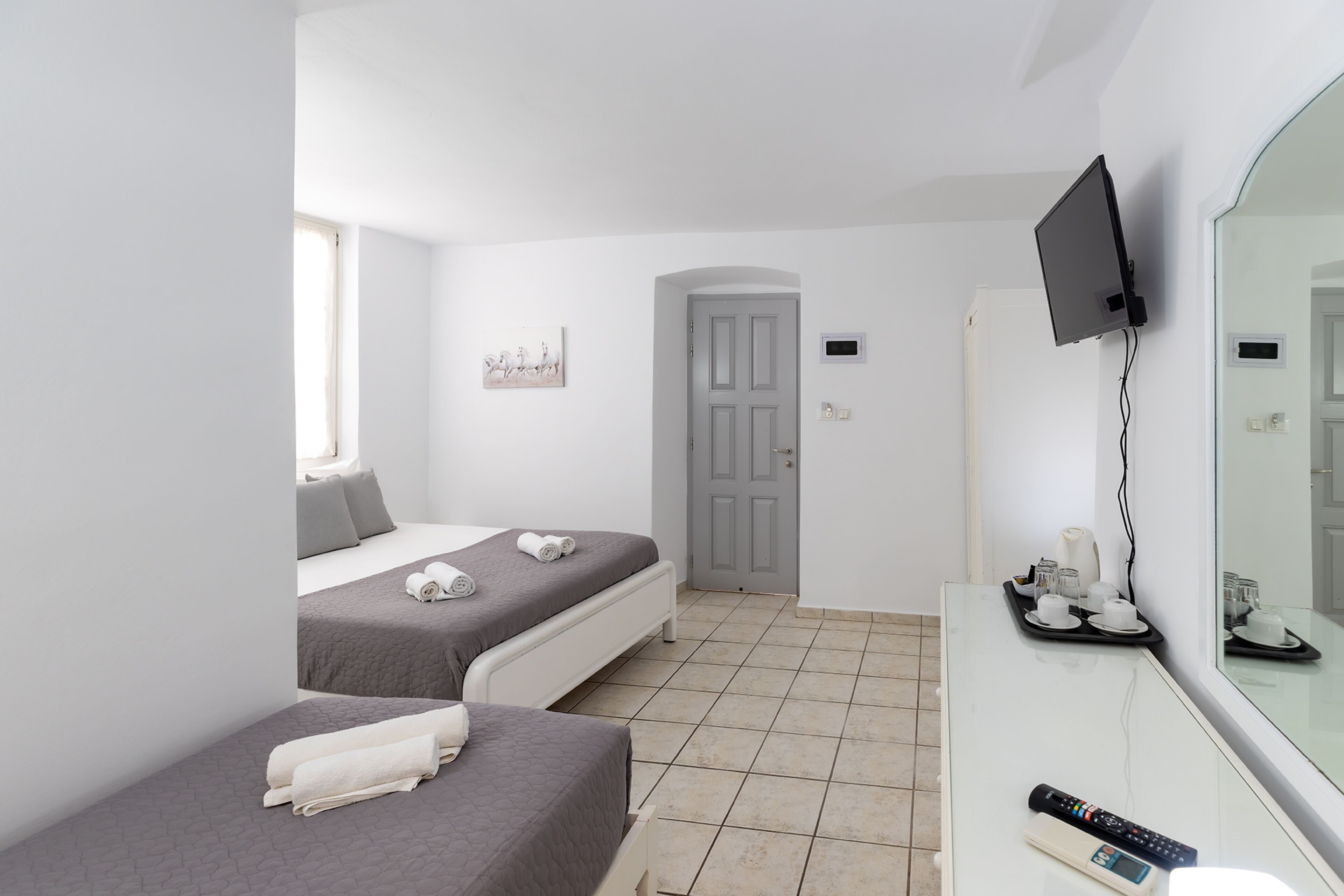 A hotel room with two beds, a TV mounted on the wall, a desk with a remote control, and a door.