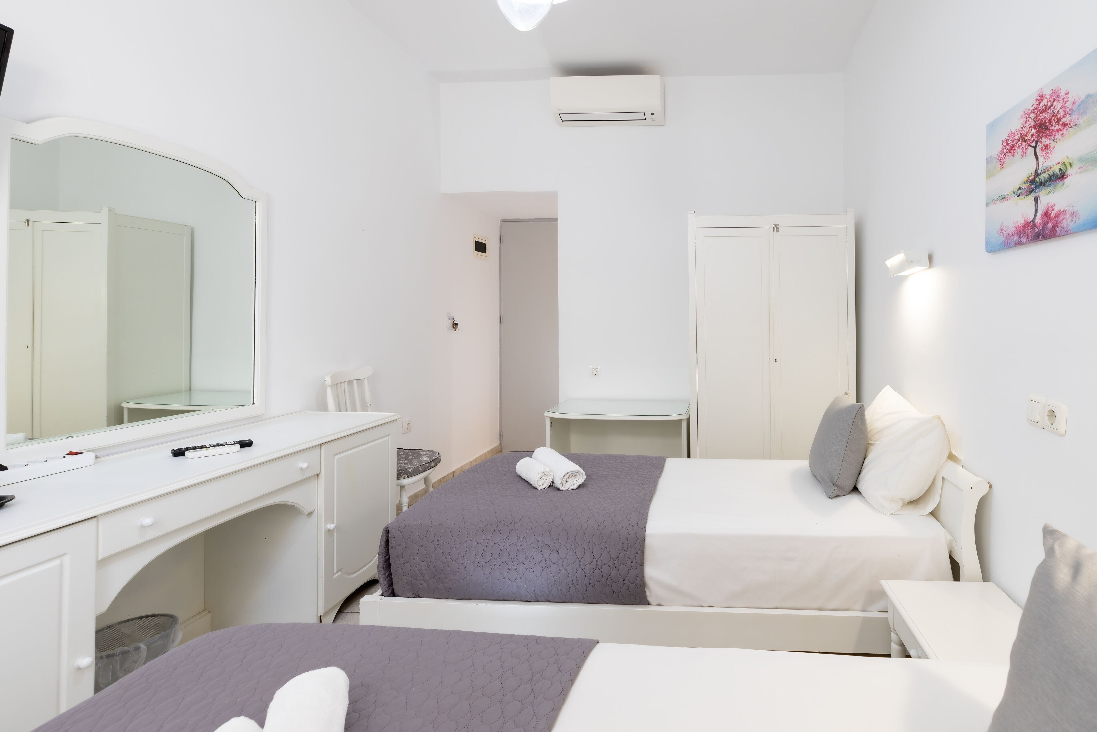 Habitación de hotel con dos camas, un escritorio, una silla, un espejo y un cuadro en la pared.