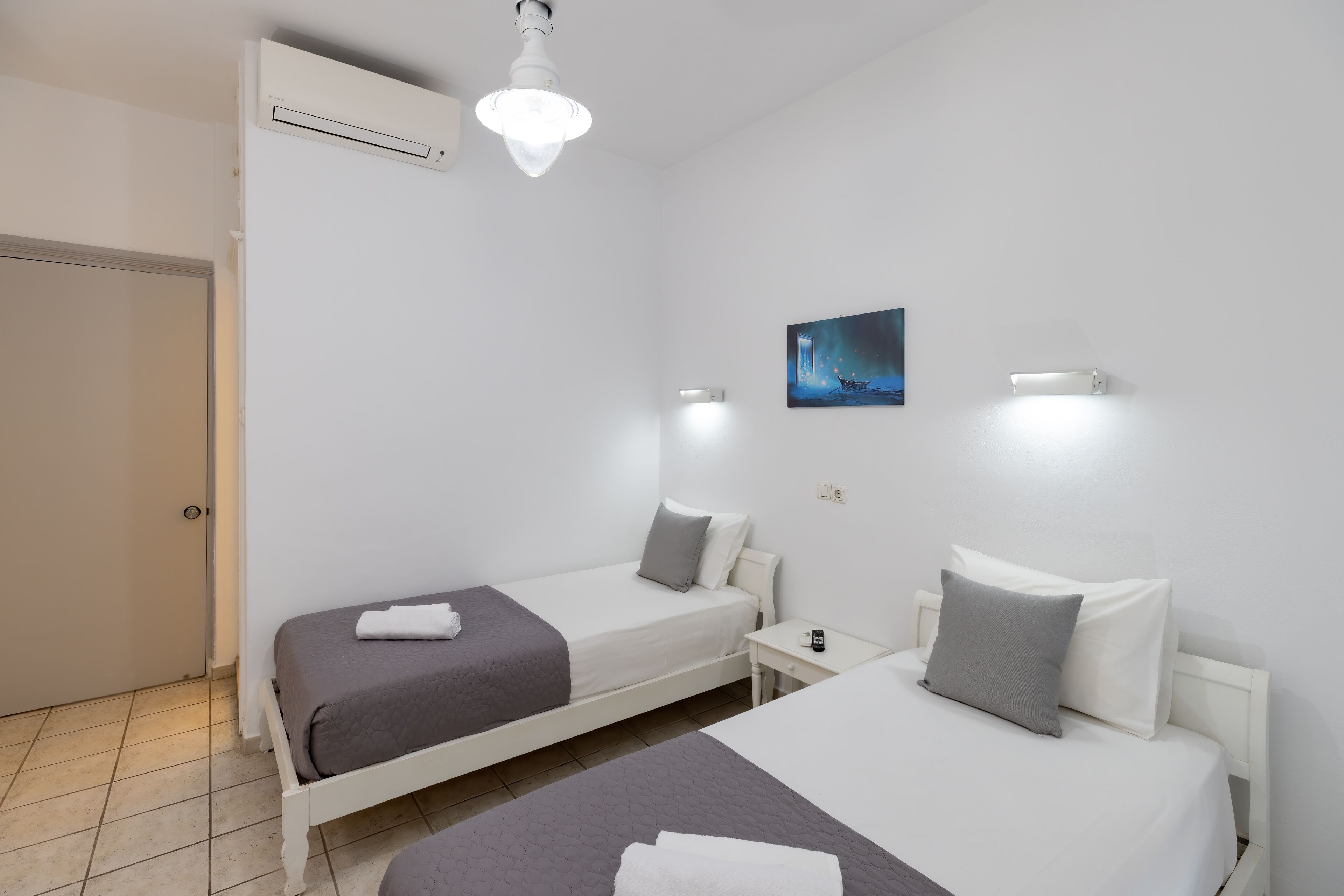 A hotel room with two single beds, a nightstand, a wall-mounted light, and a painting.