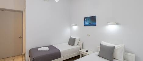 Una habitación de hotel con dos camas individuales, una mesita de noche, una lámpara de pared y un cuadro.
