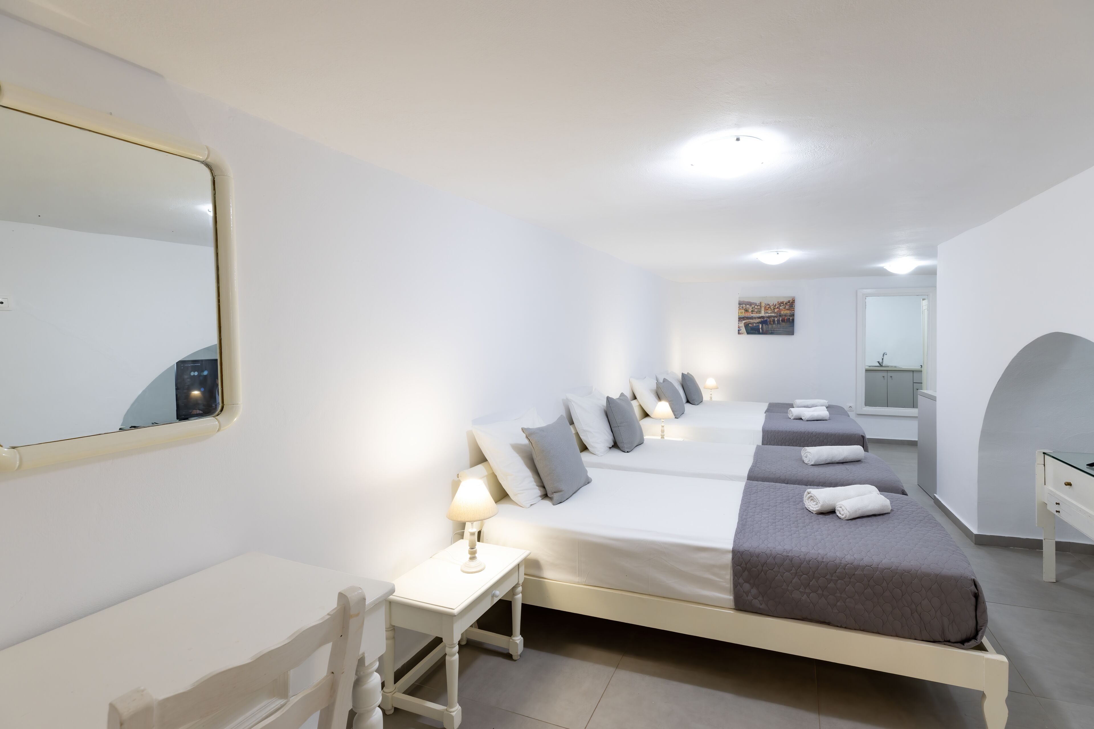 Ett hotellrum med en stor säng, ett skrivbord, en stol, en spegel och ett badrum som syns genom en valvöppning.