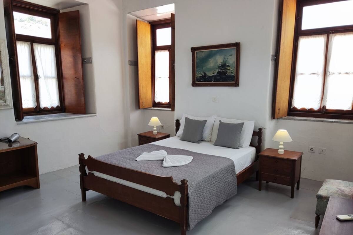Une chambre à coucher avec un lit en bois, deux tables de chevet avec des lampes, un tableau au mur et des fenêtres avec des rideaux.