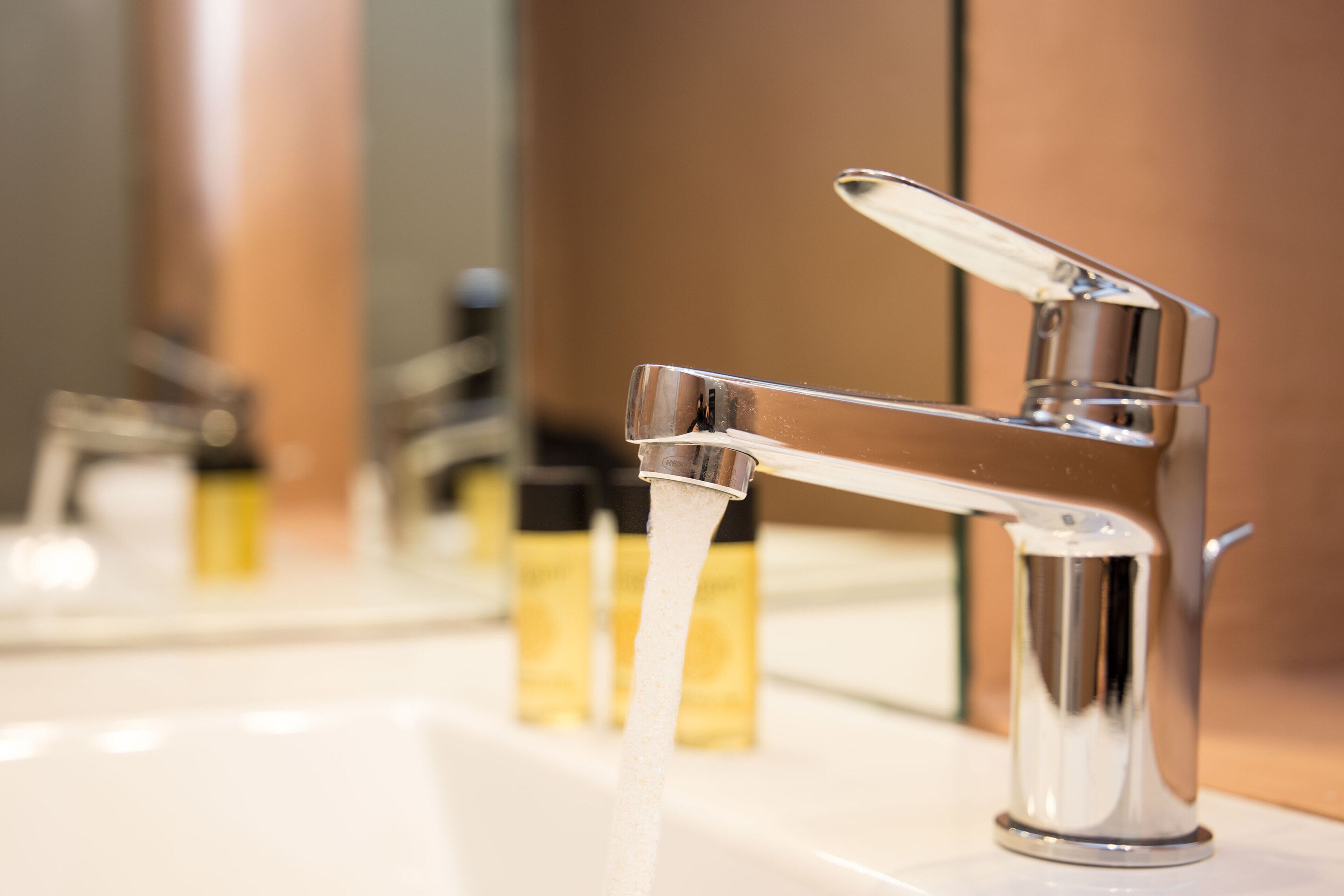 A modern bathroom with a chrome faucet and a mirror reflecting the sink and faucet.