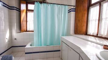 A bathroom with a bathtub, a sink, and a window with curtains.