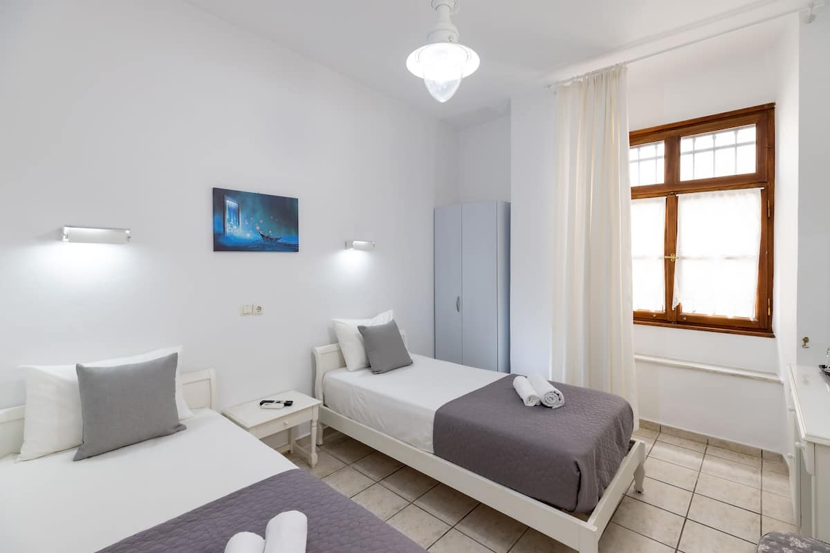 Une chambre d’hôtel avec deux lits, une table de chevet, une armoire, une fenêtre avec des rideaux et un tableau au mur.
