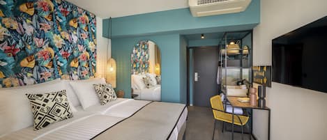 Una habitación de hotel moderna con una cama grande, un escritorio con silla, un tapiz floral llamativo y un espejo.