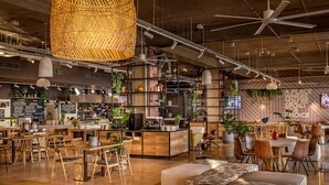 Un interior de restaurante moderno con mesas y sillas de madera, una zona de bar y diversas plantas.