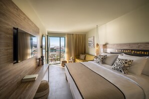 Una habitación de hotel moderna con una cama grande, un televisor de pantalla plana, un balcón con vistas y un cartel en la cabecera que dice "EJAKAI PLACES".