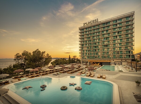 Un hotel con piscina, sillas de descanso y sombrillas.