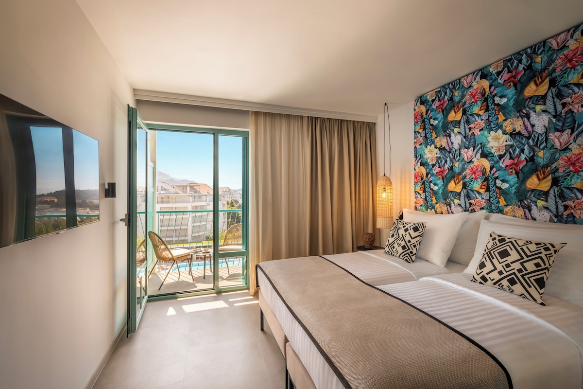 Habitación de hotel con cama, sofá, vistas a la ciudad y balcón con una silla.