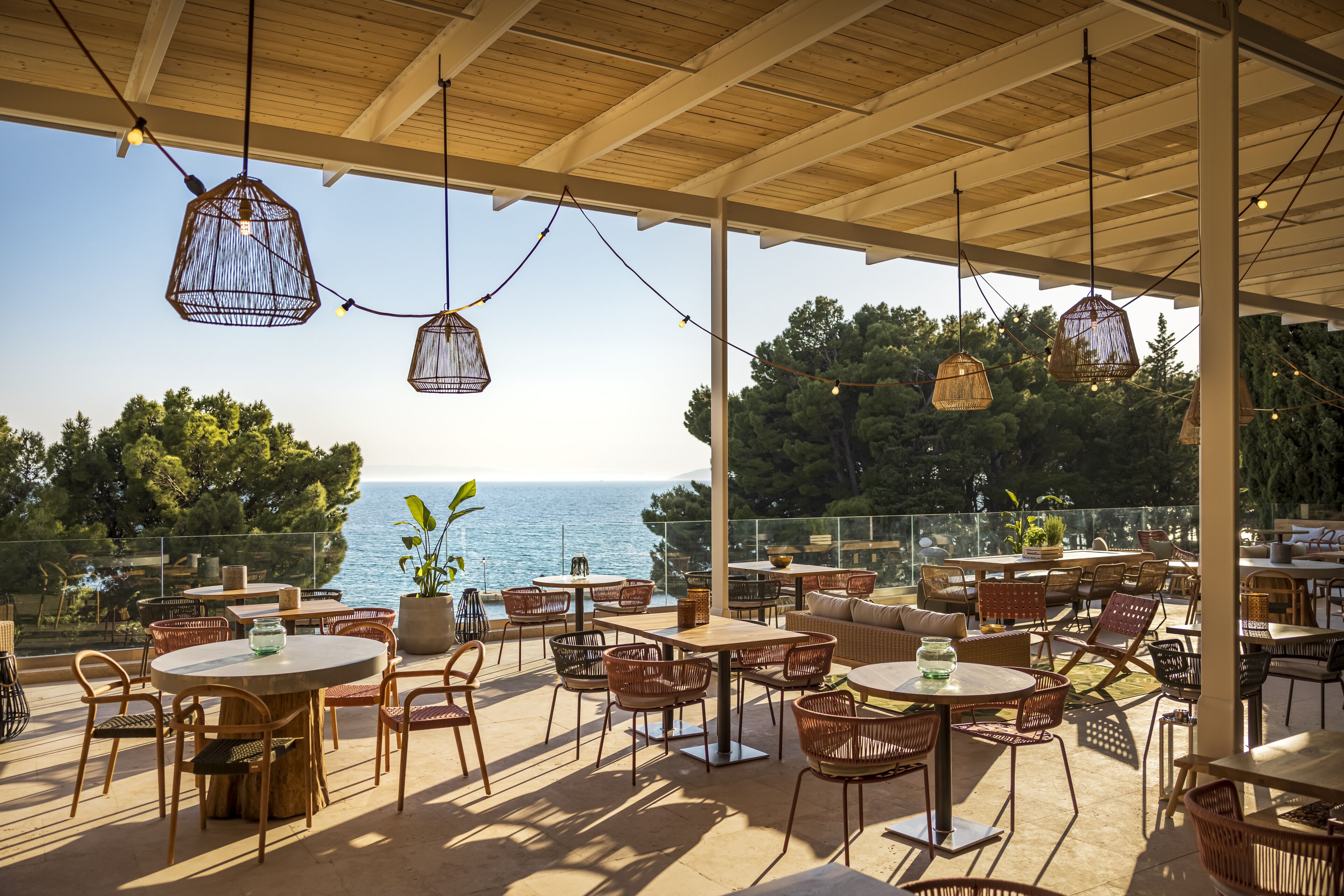 Un patio al aire libre con mobiliario de mimbre, luces colgantes y vista al mar.