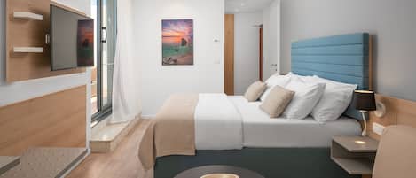 Une chambre d’hôtel moderne, équipée d’un lit, d’une table de chevet, d’une lampe et offrant une vue sur l’océan grâce à une grande fenêtre.