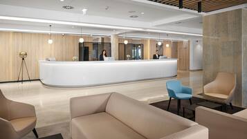 A modern reception area with a curved white counter, two receptionists, and a seating area with beige and blue chairs.