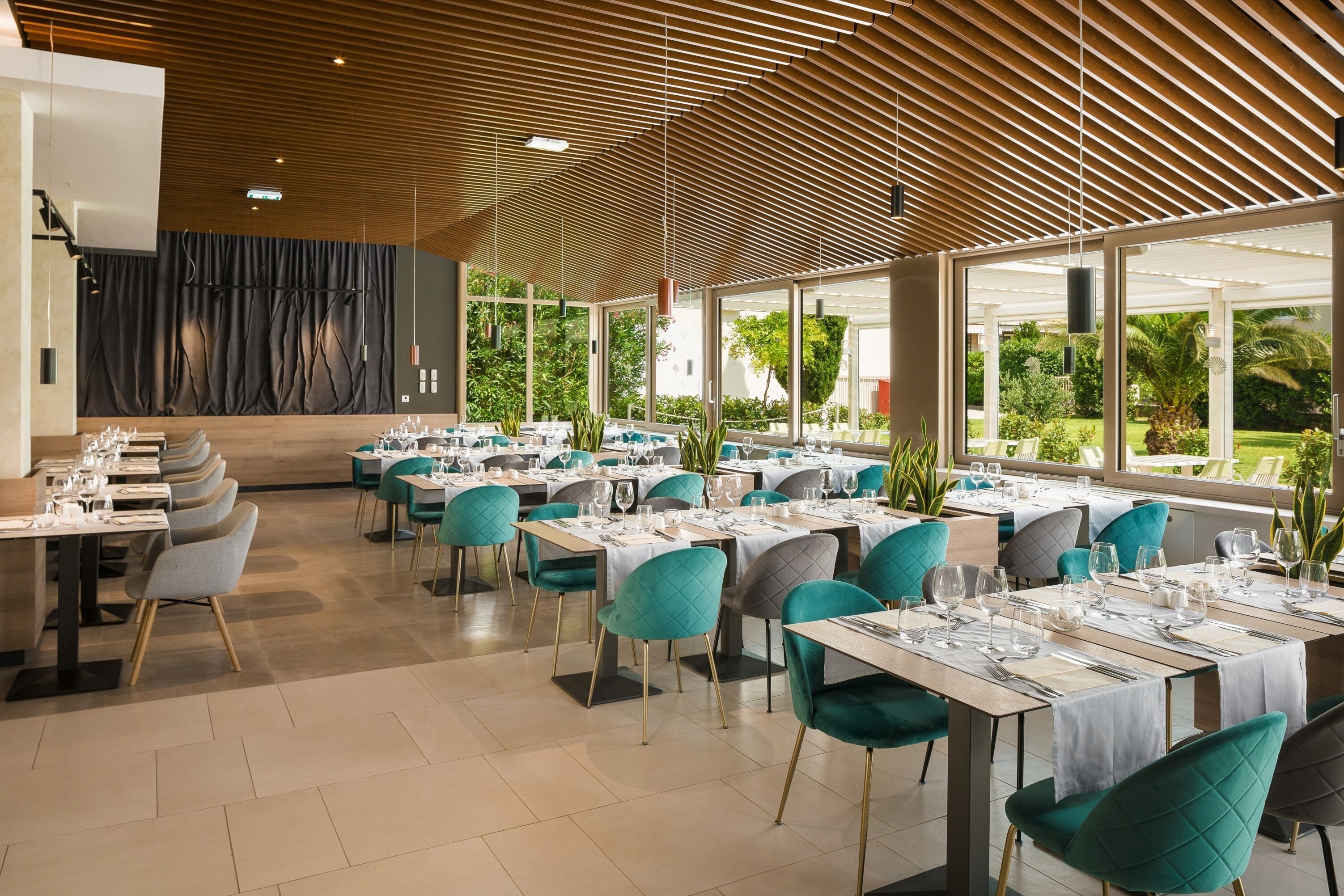 A modern restaurant with a wooden ceiling, large windows, and teal chairs.