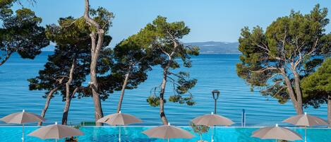 A poolside area with lounge chairs and umbrellas, overlooking a clear blue sea.