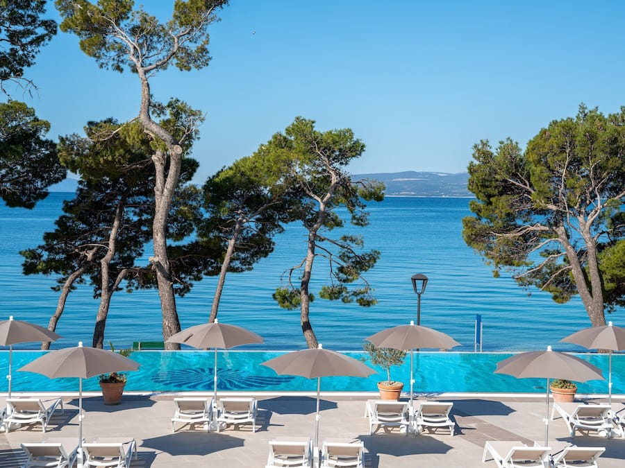 Area piscina con lettini e ombrelloni, con vista su un mare cristallino e blu.