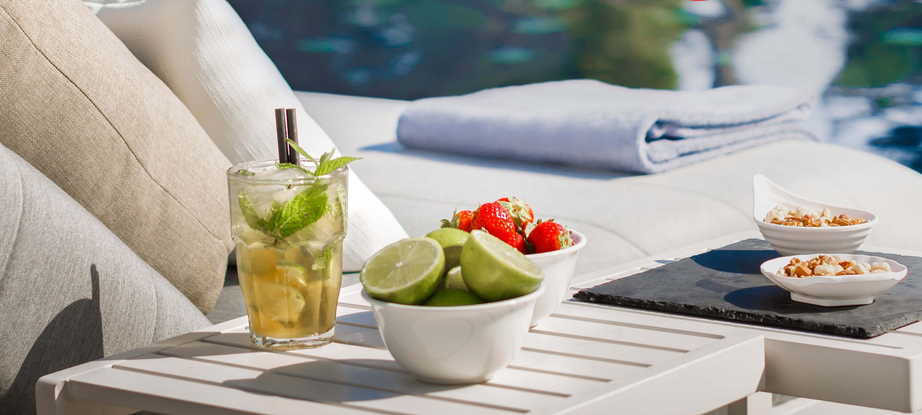 A sun lounger with a tray containing a drink, lime slices, strawberries, and a bowl of nuts.